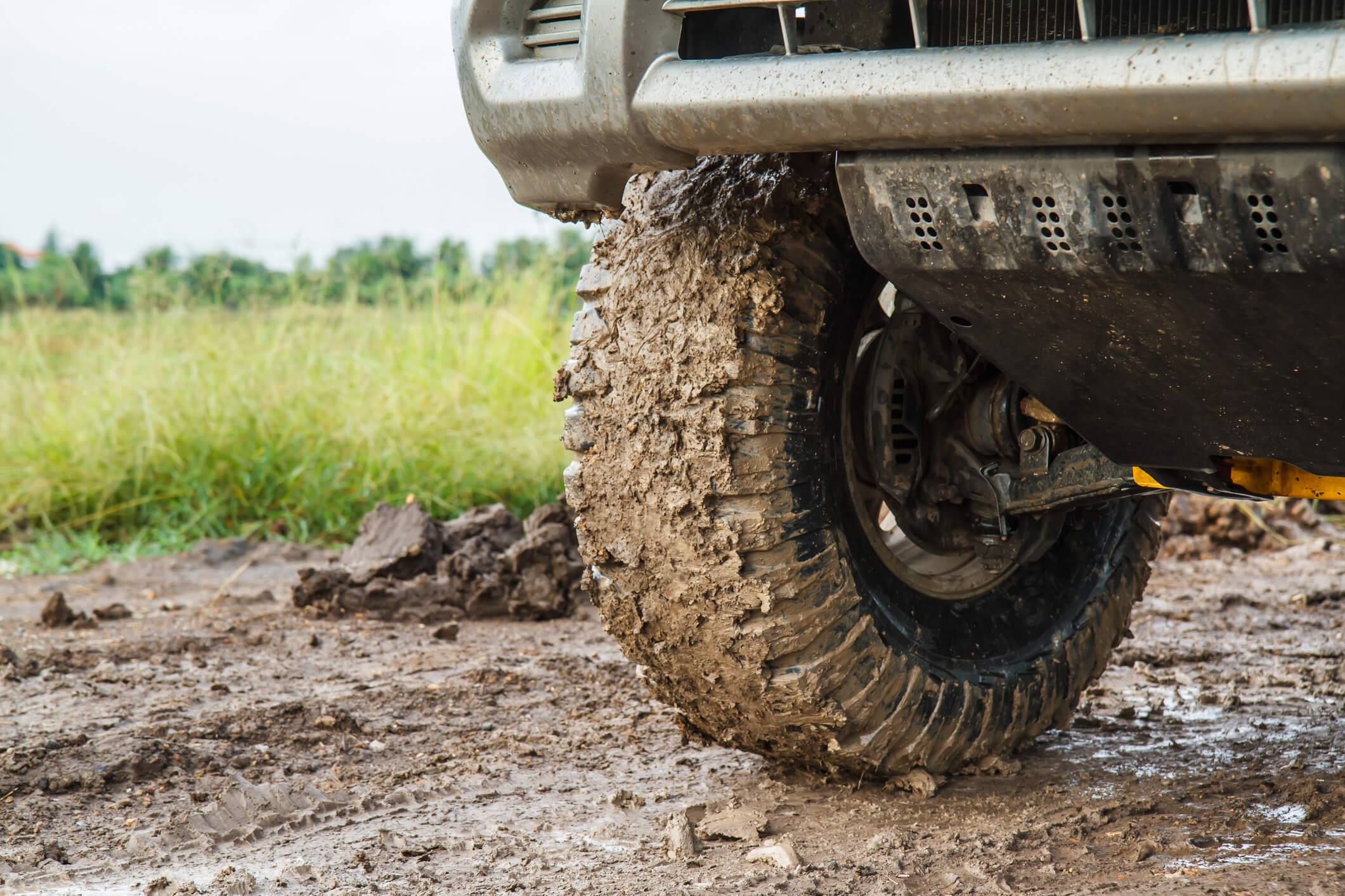 Up-close shot of the tires of an upgraded, off-road Subaru, covered in mud. A grassy field is in the background.